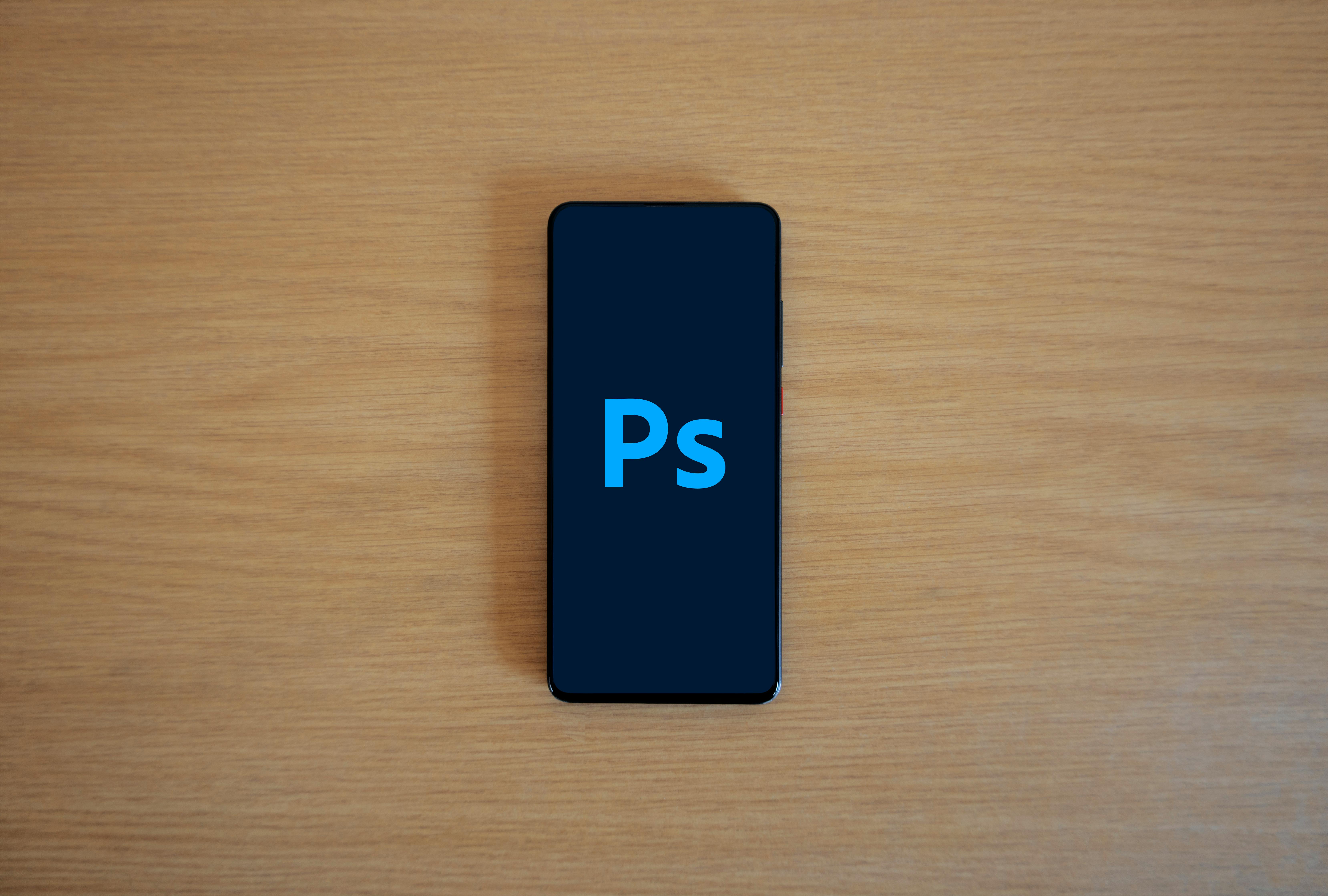 Top view of a smartphone showing Adobe Photoshop on a wooden surface.