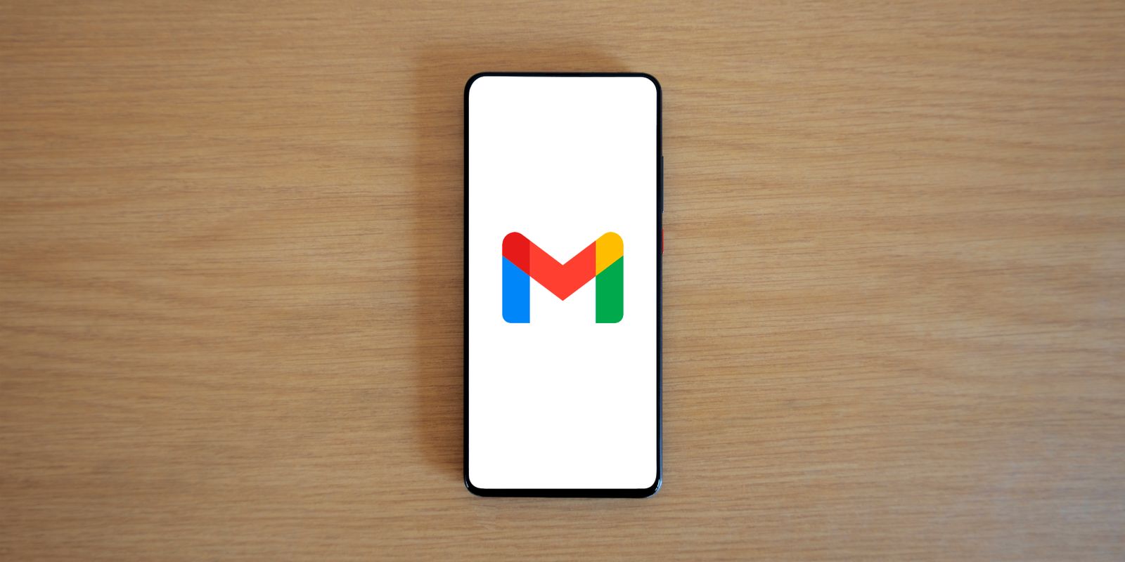 A smartphone displaying the Gmail app logo, resting on a wooden desk