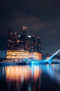 Beautiful cityscape at night featuring skyscrapers and a lit bridge reflecting over a river.