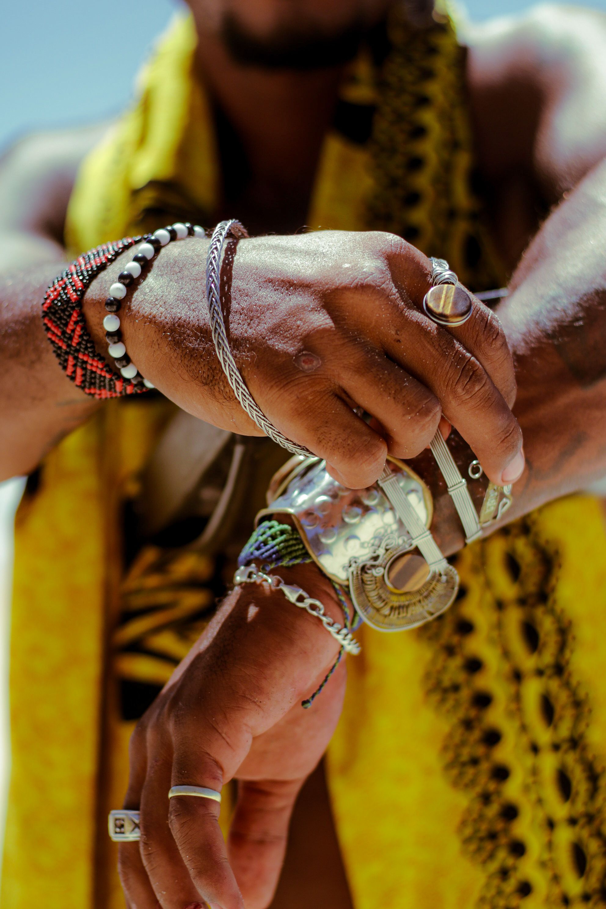 Blog, Guides bracelets - Mains d'homme portant un empilage de bracelets perlés et tissés avec bagues, mise en scène en extérieur