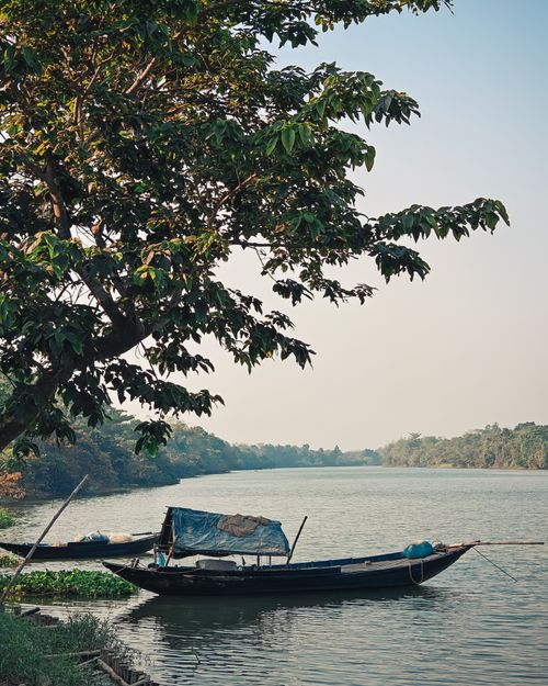 Free Tranquil river scene in Garchumbak, India, featuring a boat and lush greenery under a clear sky. Stock Photo