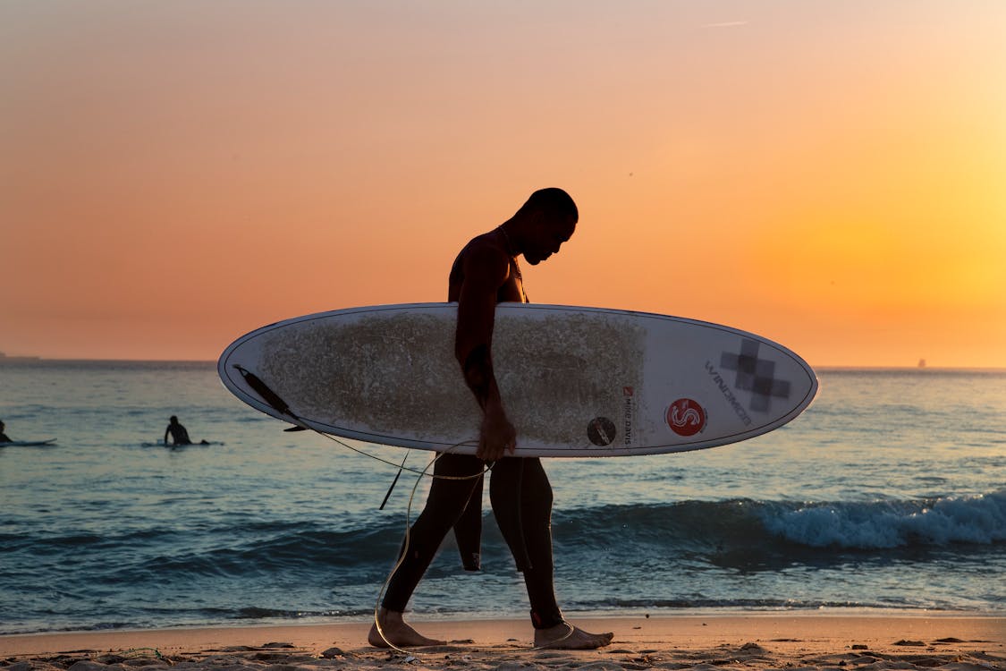 Free Man Carrying White Surfboard on Beach Stock Photo