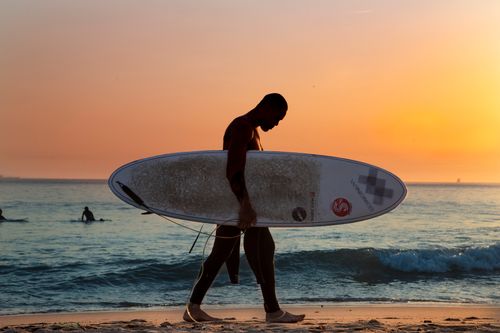 Free A surfer walks along Porto's beach with a surfboard at sunset, capturing the essence of seaside adventure. Stock Photo