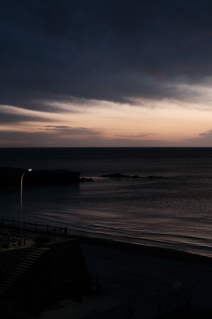 Dramatic sunset over the ocean with dark storm clouds and a serene shoreline.