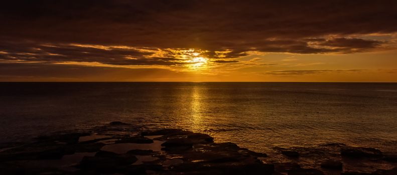 Golden sunset reflecting on the ocean waves near a rocky shore.