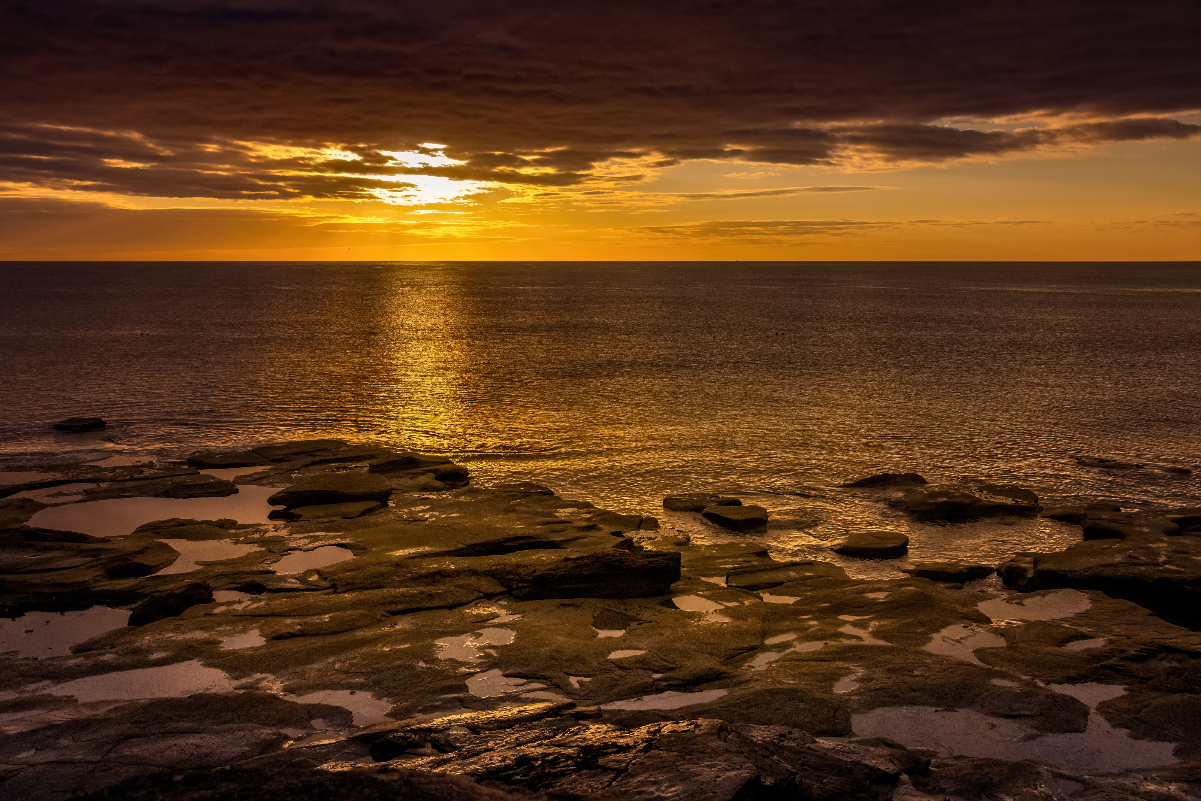 A sunset over the ocean with rocks and water · Free Stock Photo