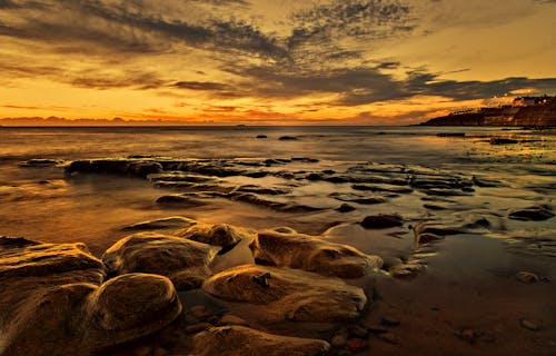 Yellow Sky over Rocks on Sea Shore at Sunset