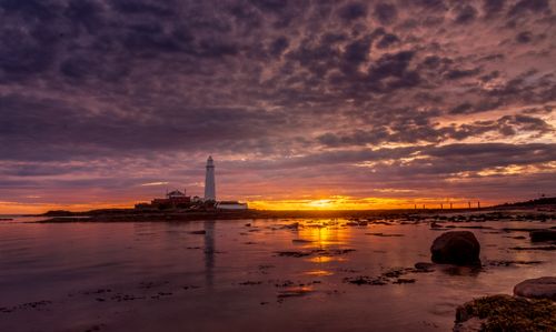 Free Stunning sunset over a lighthouse by the ocean with dramatic skies and rocky shoreline. Stock Photo