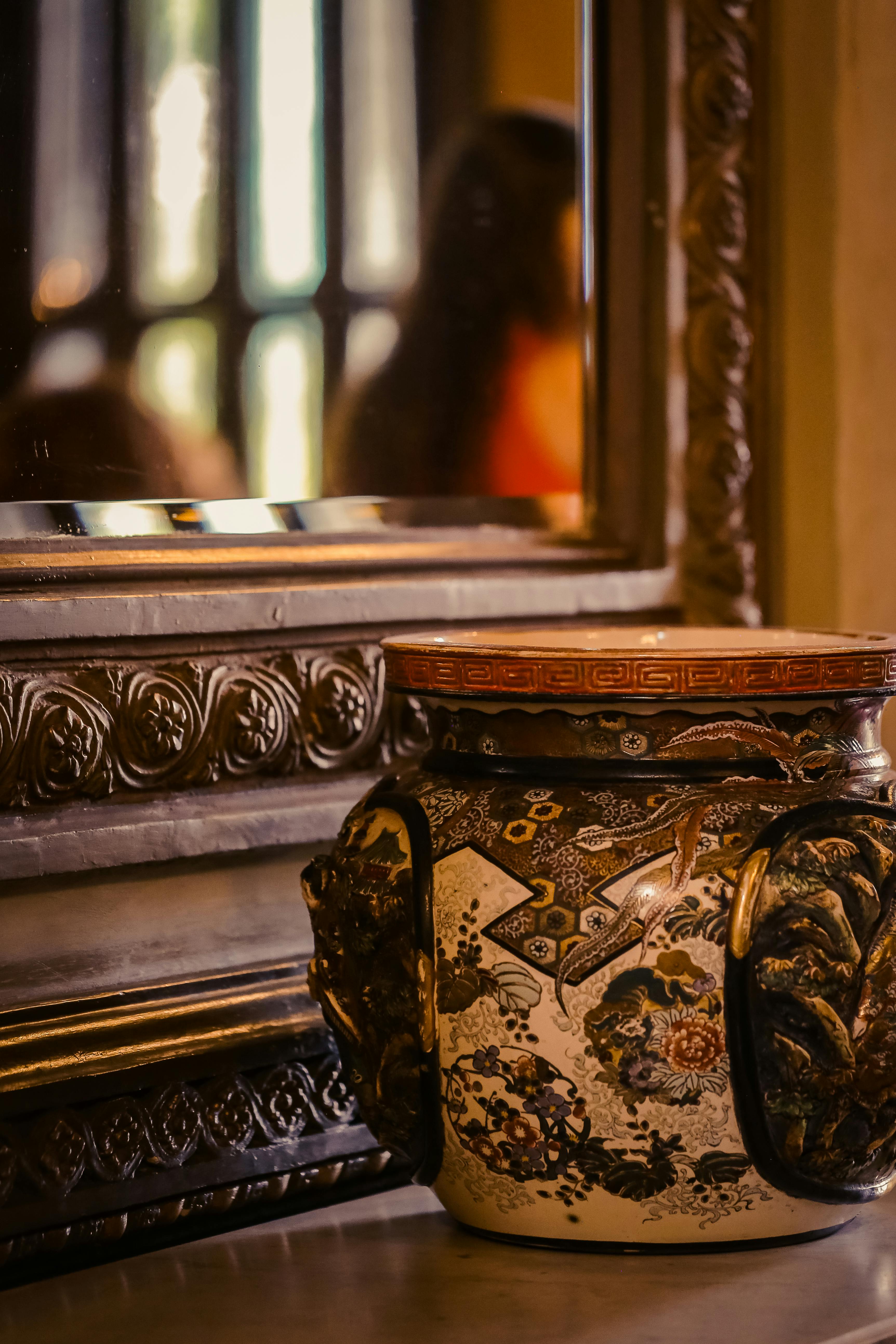 Elegant decorative vase with intricate patterns next to an ornate mirror indoors.