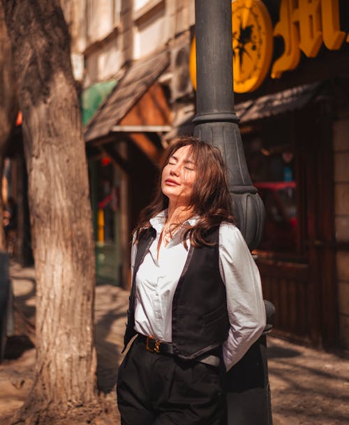 A woman leaning against a lamp post in a city