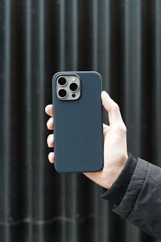 Hand holding a smartphone in a sleek black case against a dark background.