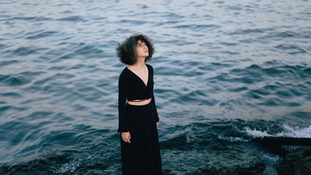 Young Woman Wearing a Black Dress Standing on a Seashore
