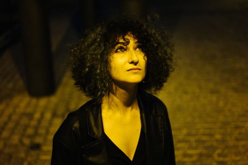 Free A woman with curly hair in a V-neck dress gazes upward under streetlights. Stock Photo