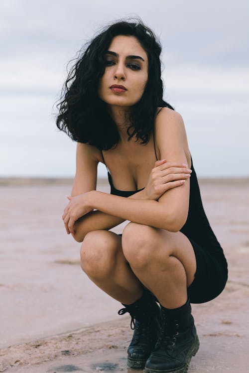 Woman with Black Hair Squatting on Beach