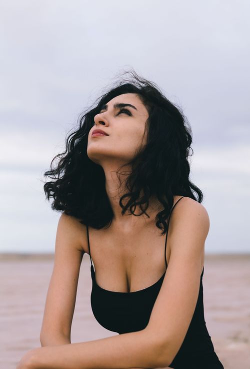 Free Portrait of a woman in a black camisole dress looking up, set against an outdoor backdrop. Stock Photo