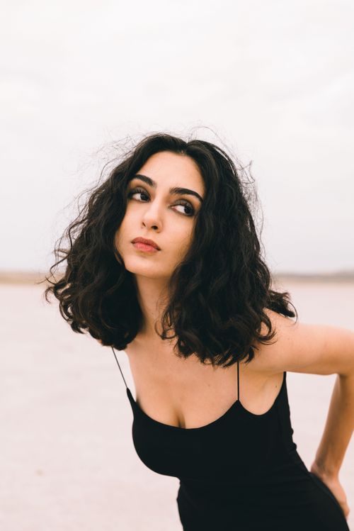Free Stylish outdoor portrait featuring a woman in a black dress with curly hair, captured during the day. Stock Photo