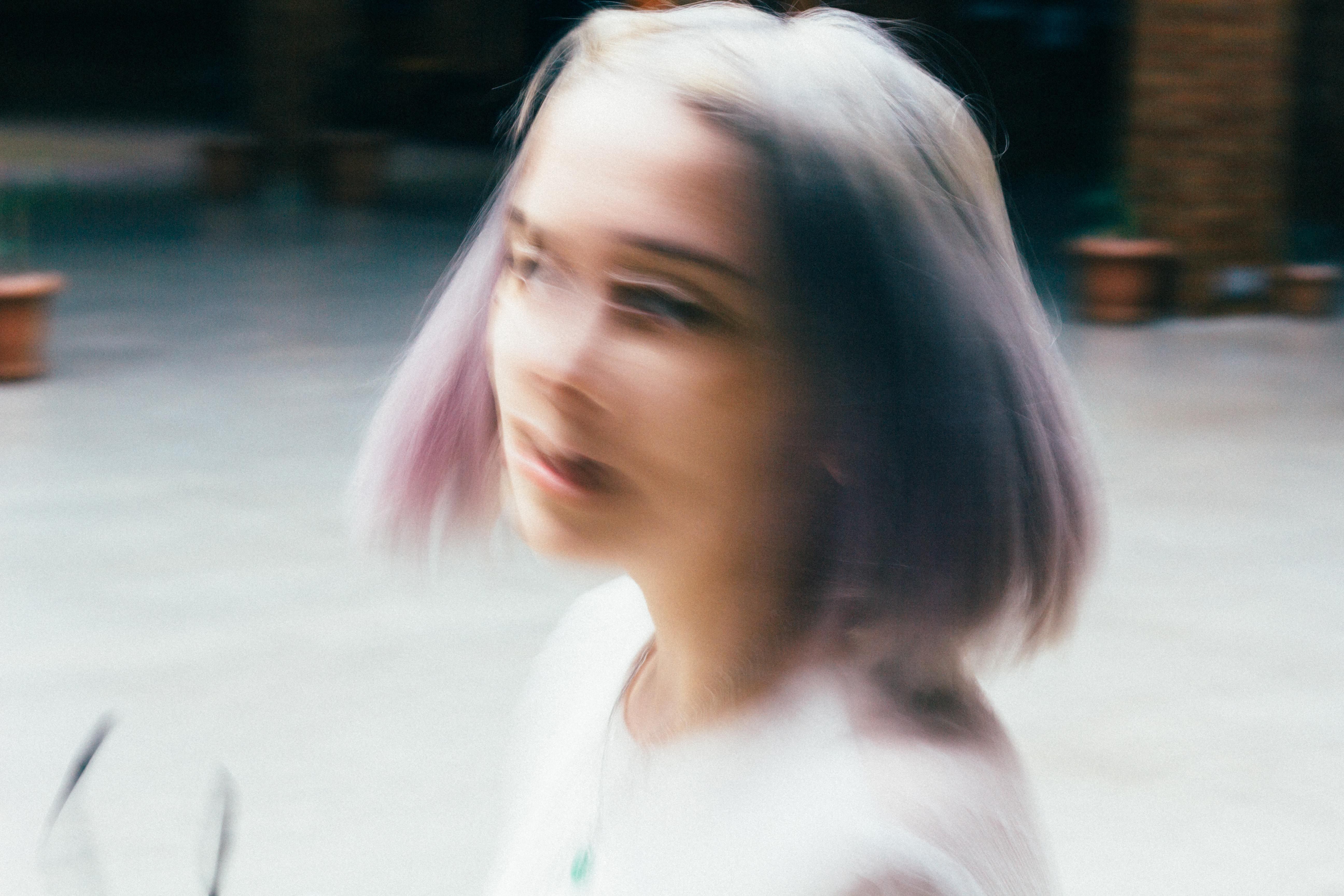 Dynamic blurred portrait of a young woman with dyed purple hair outdoors.