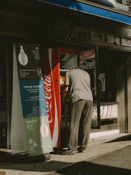 Free A man checks a Coca-Cola vending machine in a bustling city street scene. Stock Photo