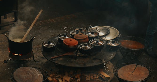 A rustic cooking setup with steaming pots and pans over an open flame.