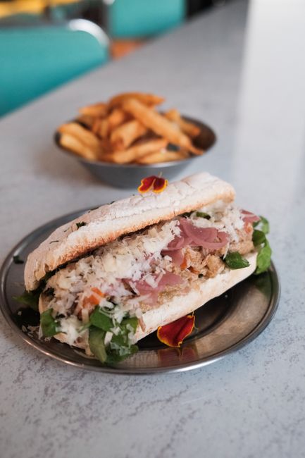 A sliced Italian sub sandwich showing layers of salami, capicola, provolone, shredded lettuce, tomato, and red onion on a crusty roll drizzled with oil and vinegar.