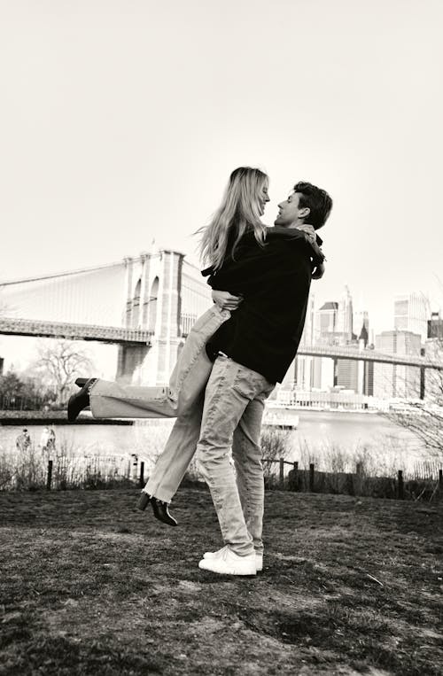A couple is hugging each other in front of the brooklyn bridge
