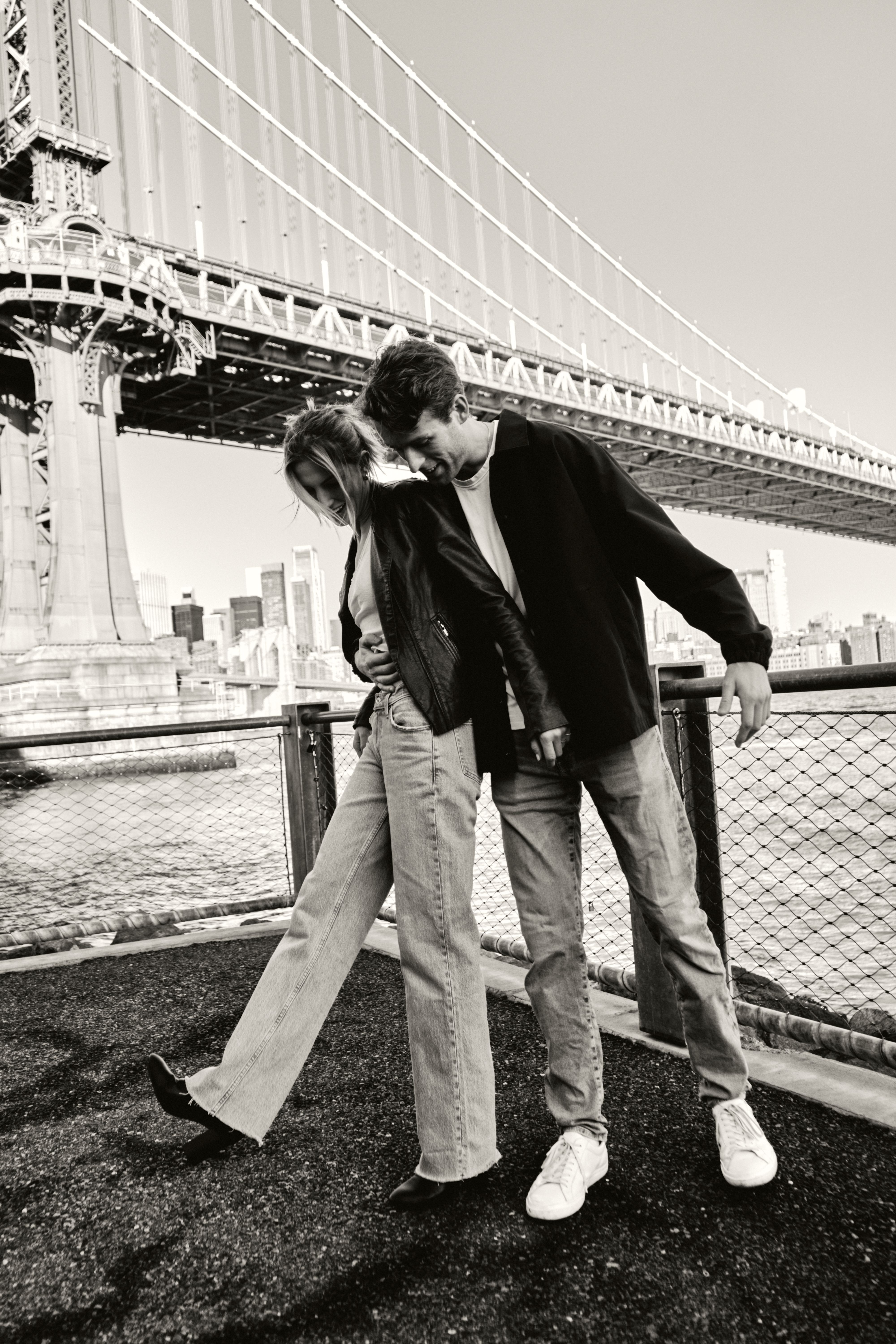 Couple in Jackets and Jeans Posing Together Near Bridge · Free Stock Photo