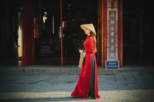 Free An Asian woman in a red dress and conical hat walking outdoors, embodying cultural elegance. Stock Photo