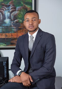 Young businessman in an elegant suit sitting in an office environment with a thoughtful expression.