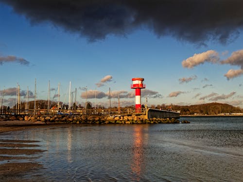 A lighthouse is on the beach with a cloudy sky