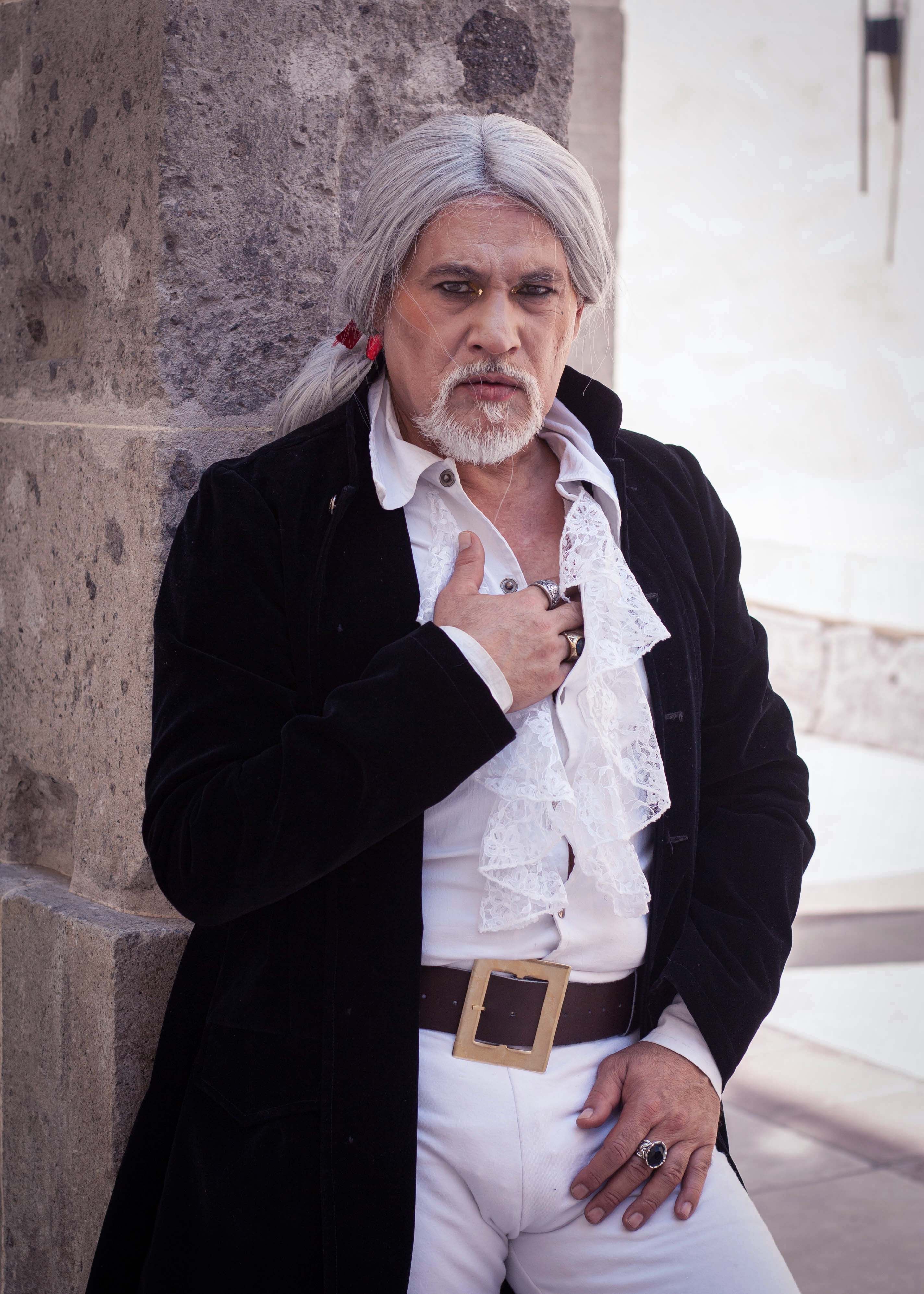 Man in historical attire with white wig and lace shirt standing by a stone pillar.