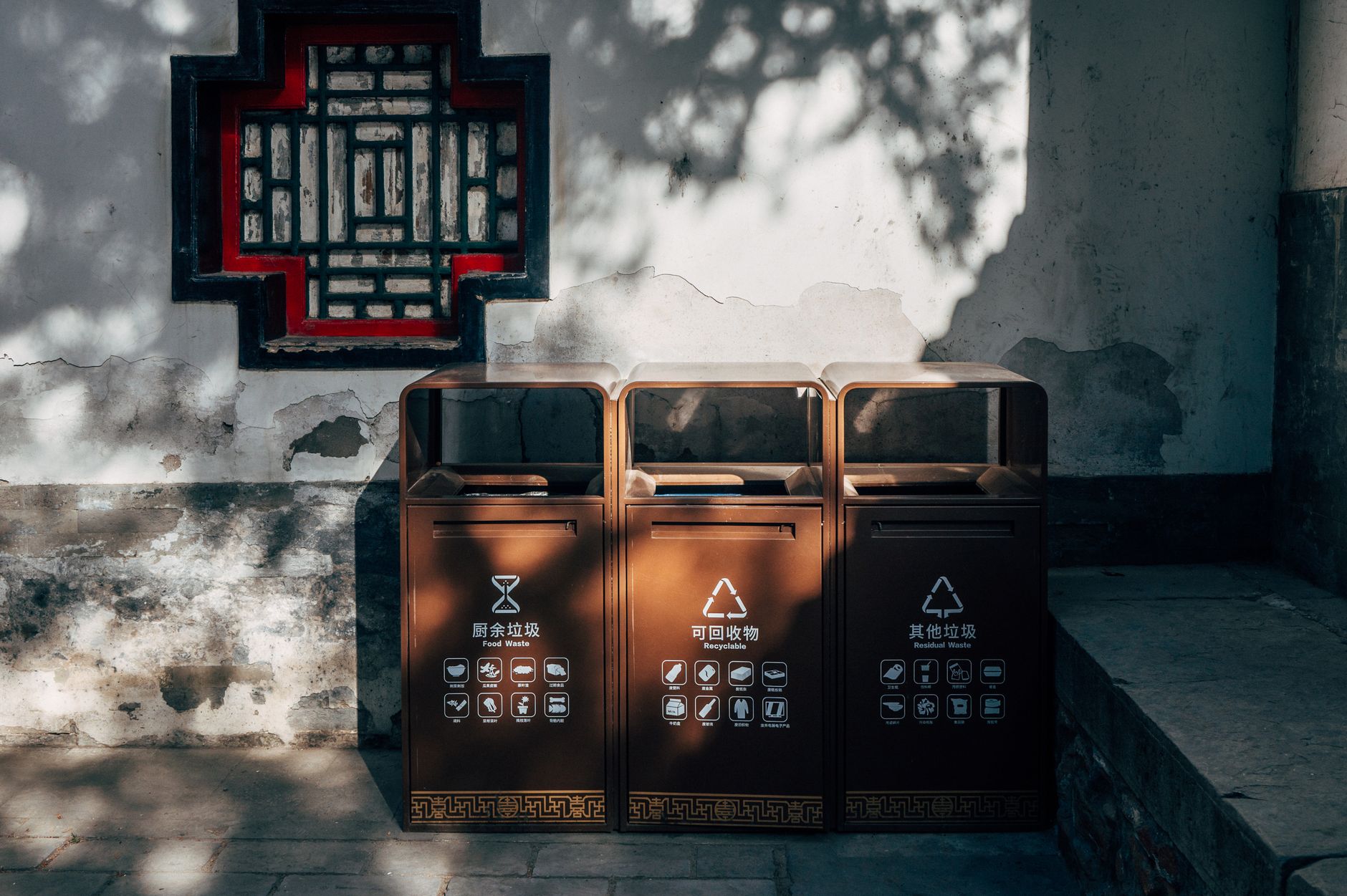 Sunlit traditional Chinese wall and recycling bins in an outdoor setting.