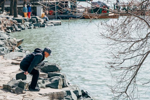 A man is kneeling on the rocks near the water