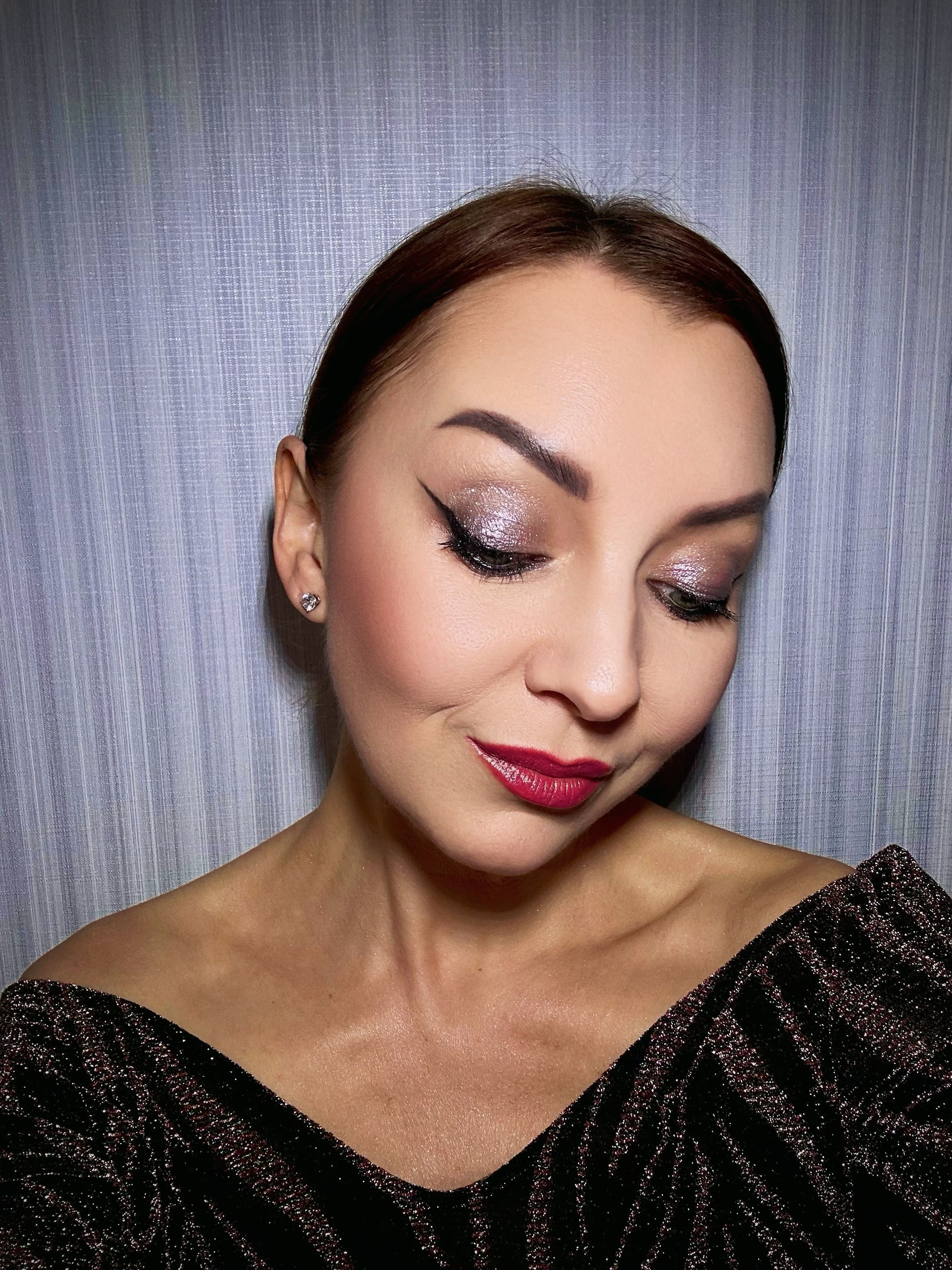 Close-up portrait featuring a woman with shimmering eye makeup and vibrant lipstick against a gray background.