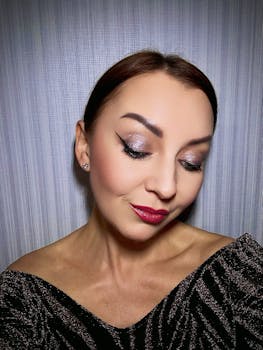 Close-up portrait featuring a woman with shimmering eye makeup and vibrant lipstick against a gray background.