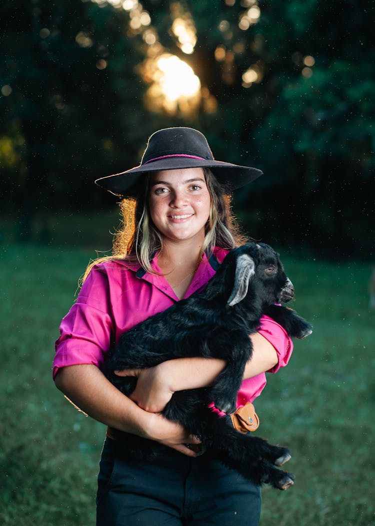 Woman Holding A Black Lamb In A Park During Sunset 