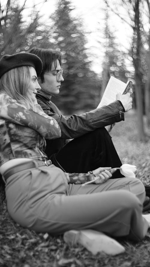 A man and woman sitting on the ground reading a book