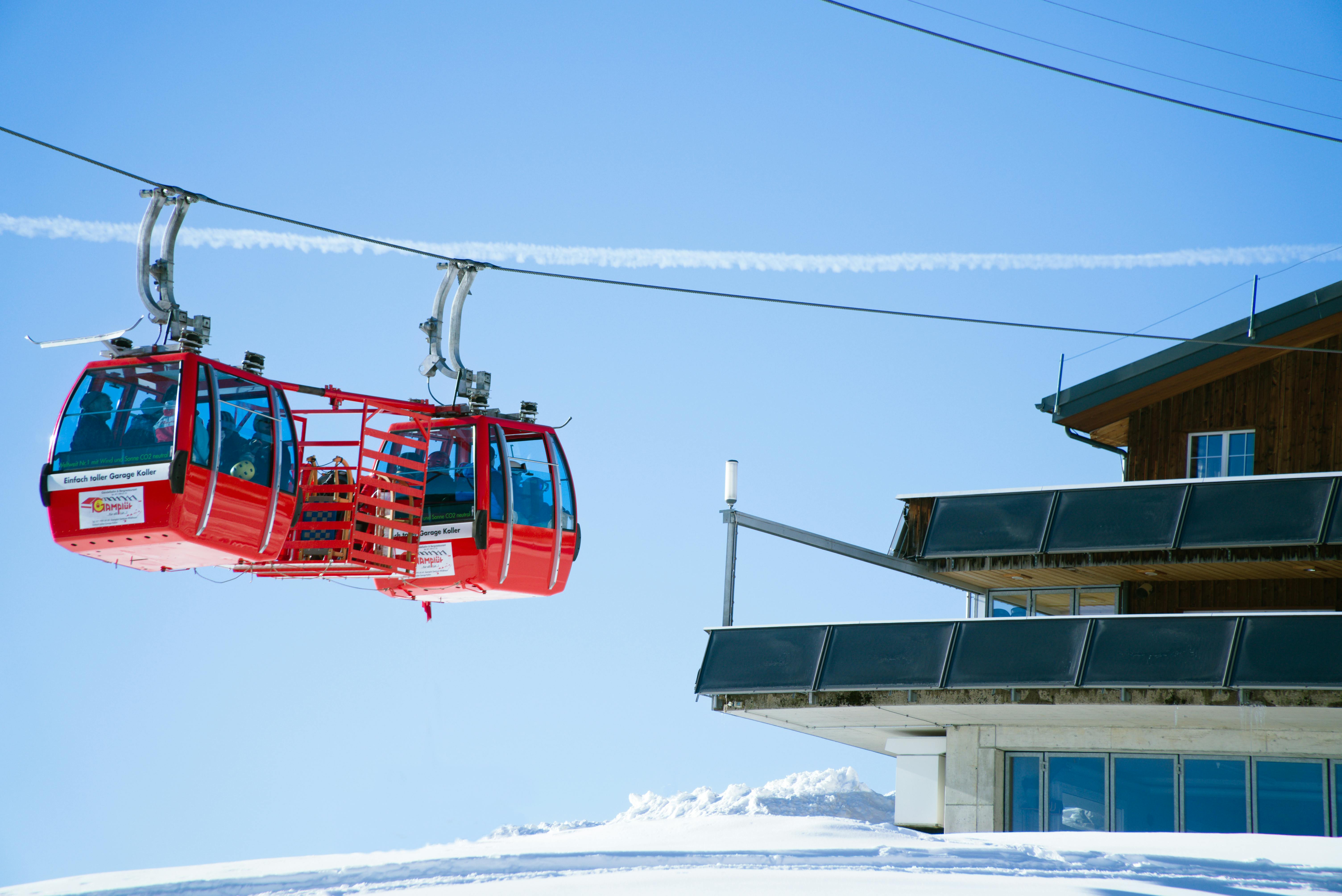 Red cable cars glide over a snowy mountain resort under a clear blue sky.