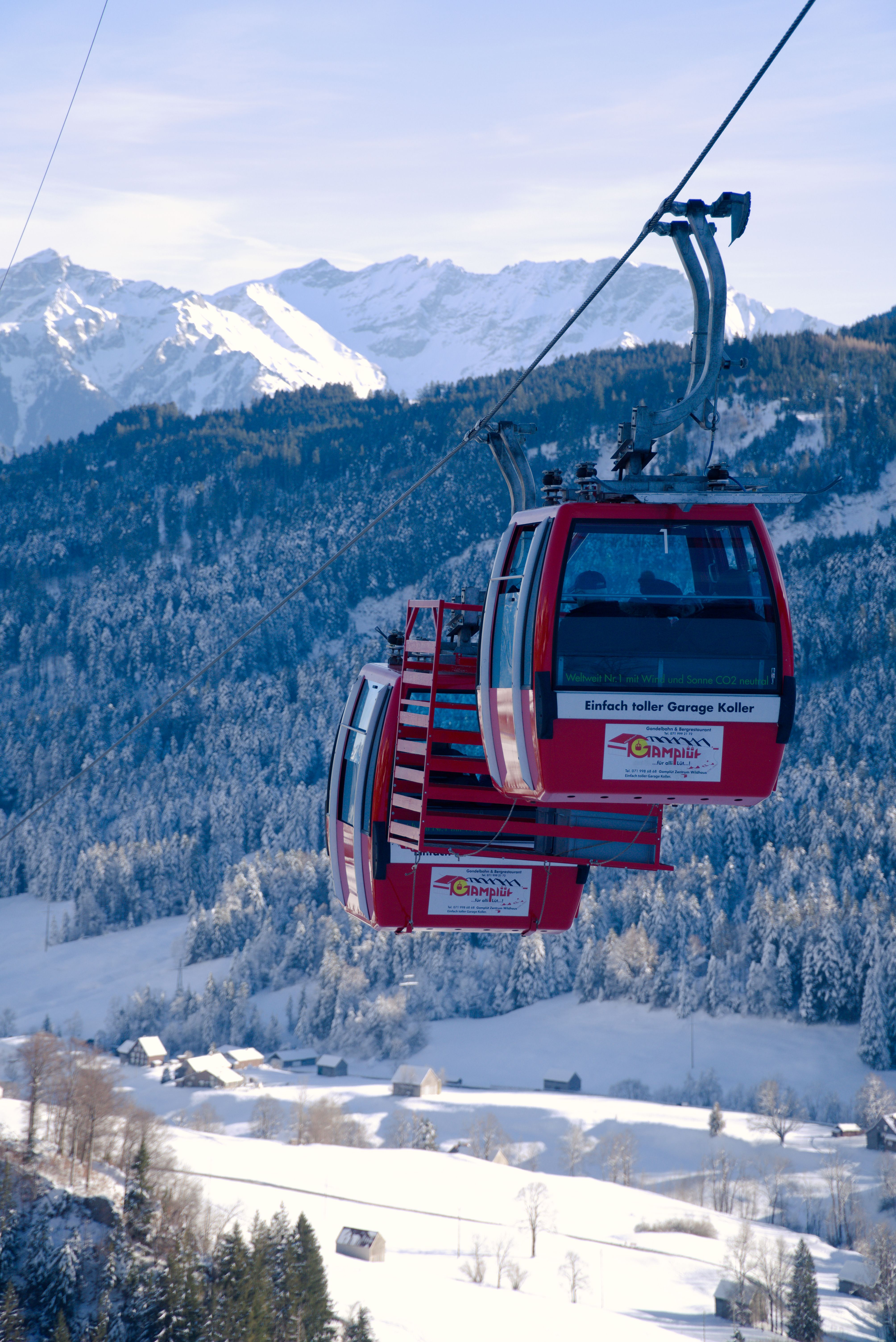 Red cable cars travel over a scenic snowy alpine landscape with mountain views.