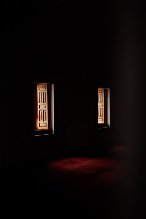 Free Serene mosque interior with two illuminated windows casting subtle light onto dark surroundings. Stock Photo