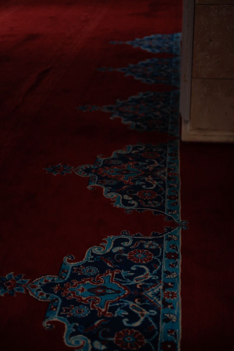 Detailed view of a beautifully patterned red carpet inside a mosque, showcasing Islamic artistry