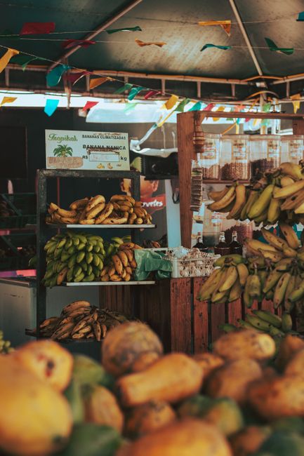 Photo by Vinicius A. Nascimento Colorful outdoor market stall displaying a variety of fresh bananas and papayas.