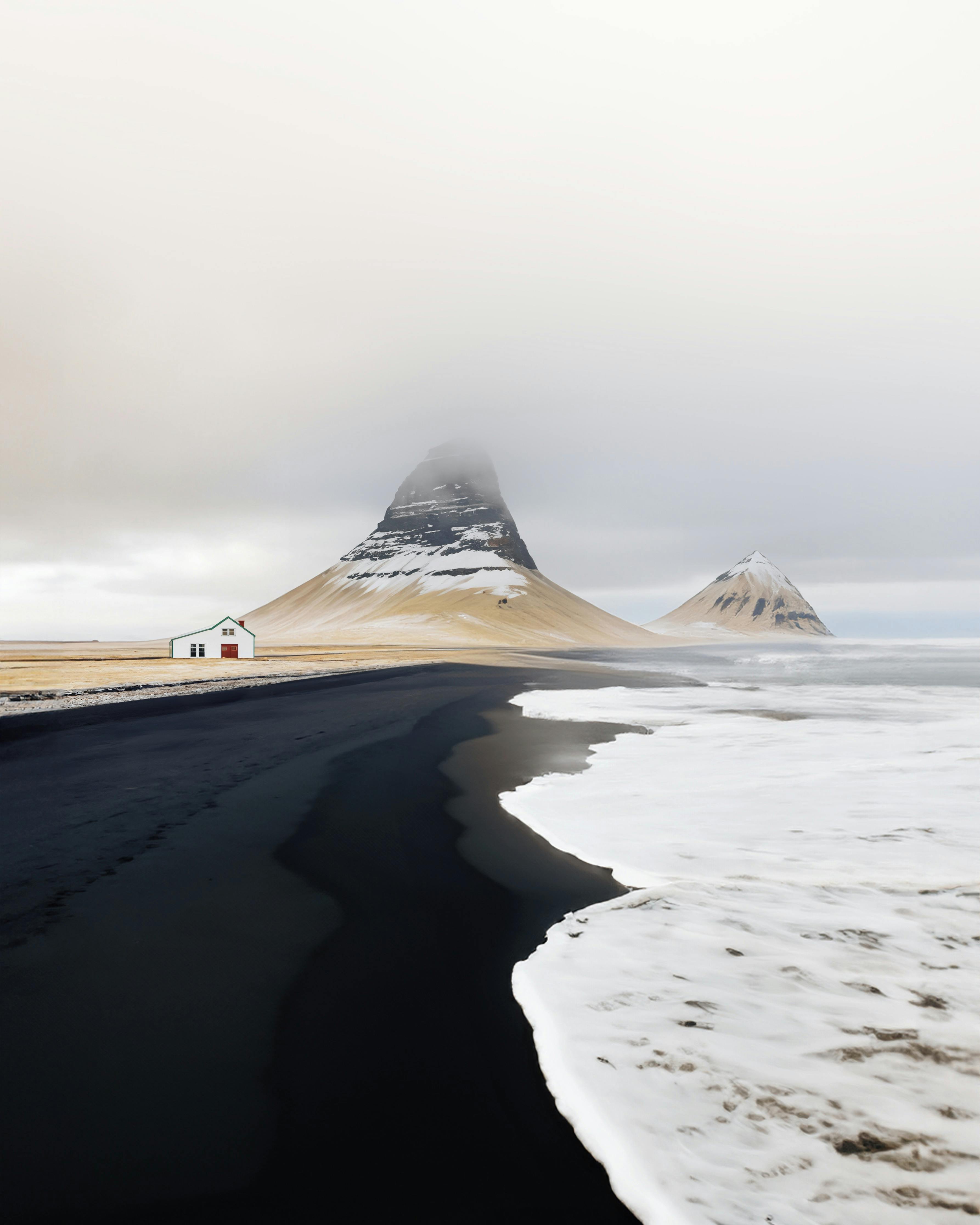Dramatic coastal scene with black sand beach and mist-covered mountain.