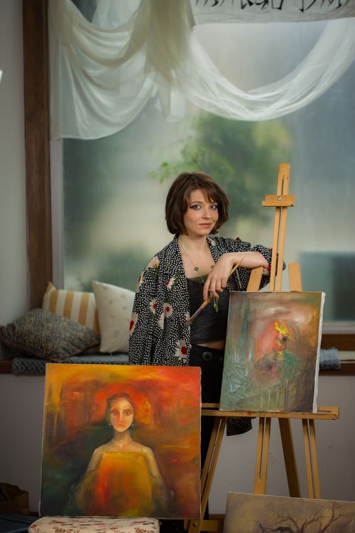 Free A woman artist stands by her easel displaying two vibrant portrait paintings. Stock Photo