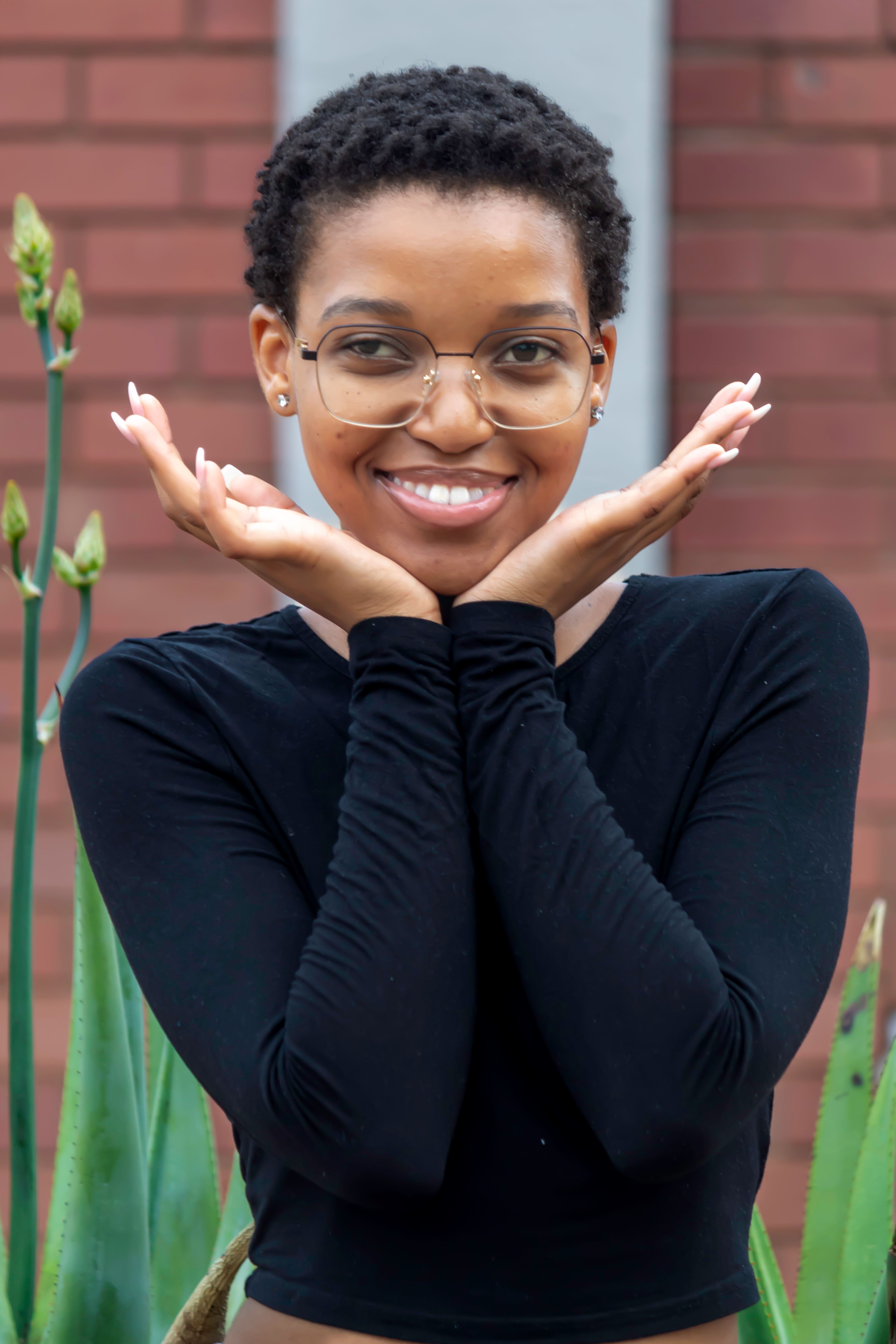 Portrait of a stylish young woman with glasses smiling outdoors, wearing a black blouse.
