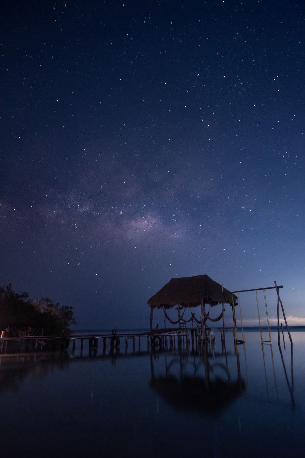 Muelle con columpios bajo un cielo estrellado sobre la laguna de Bacalar por la noche