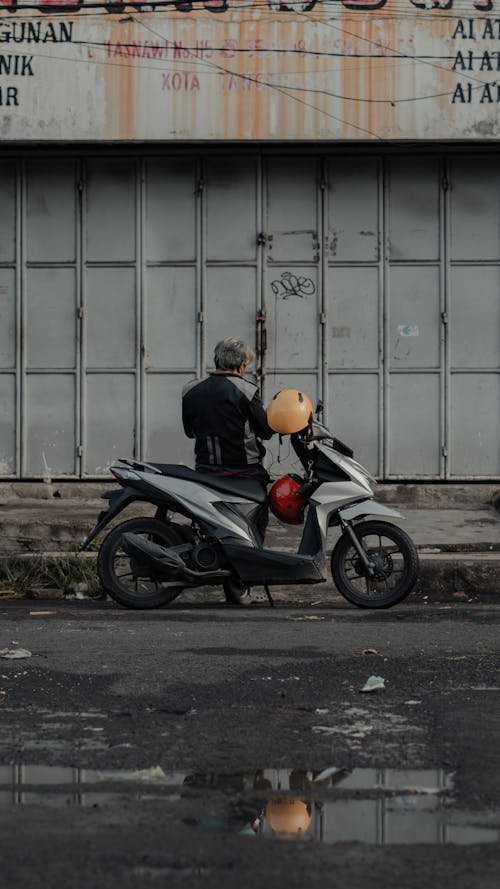 A man on a motorcycle is standing next to a building