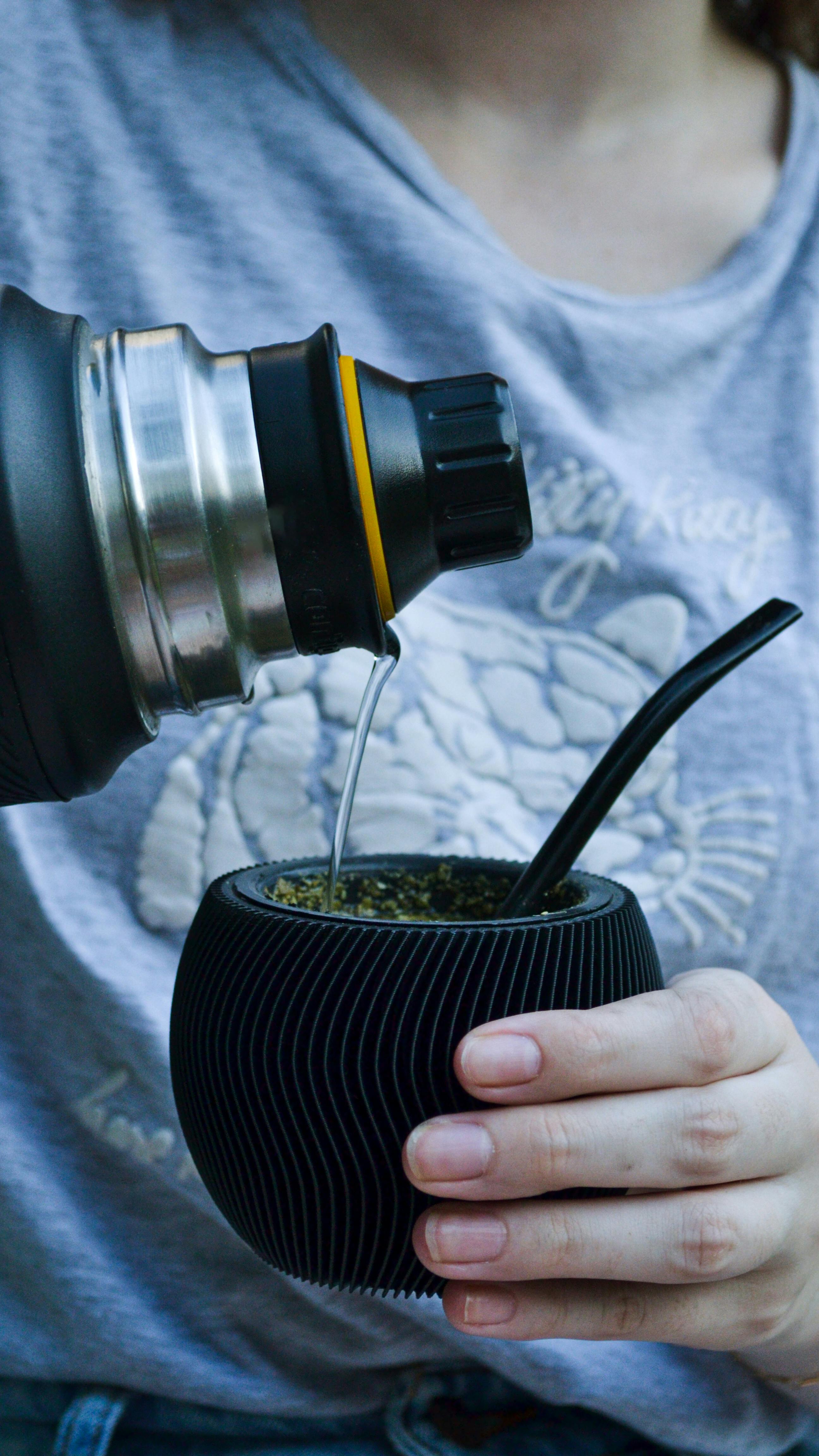 Close-up of tea being poured into a stylish yerba mate cup with straw.