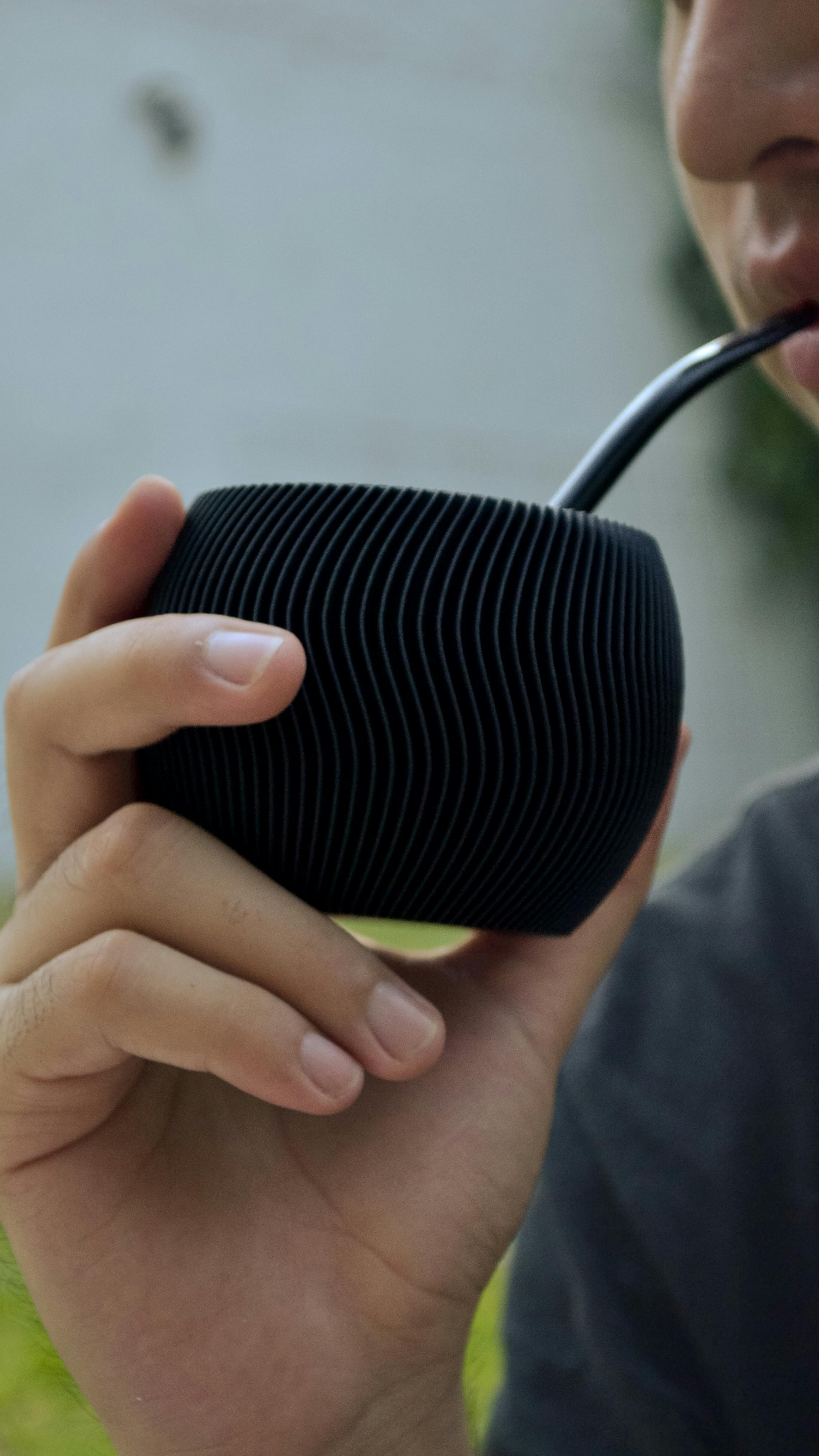 Close-up of a man drinking yerba mate from a sleek black cup, outdoors.