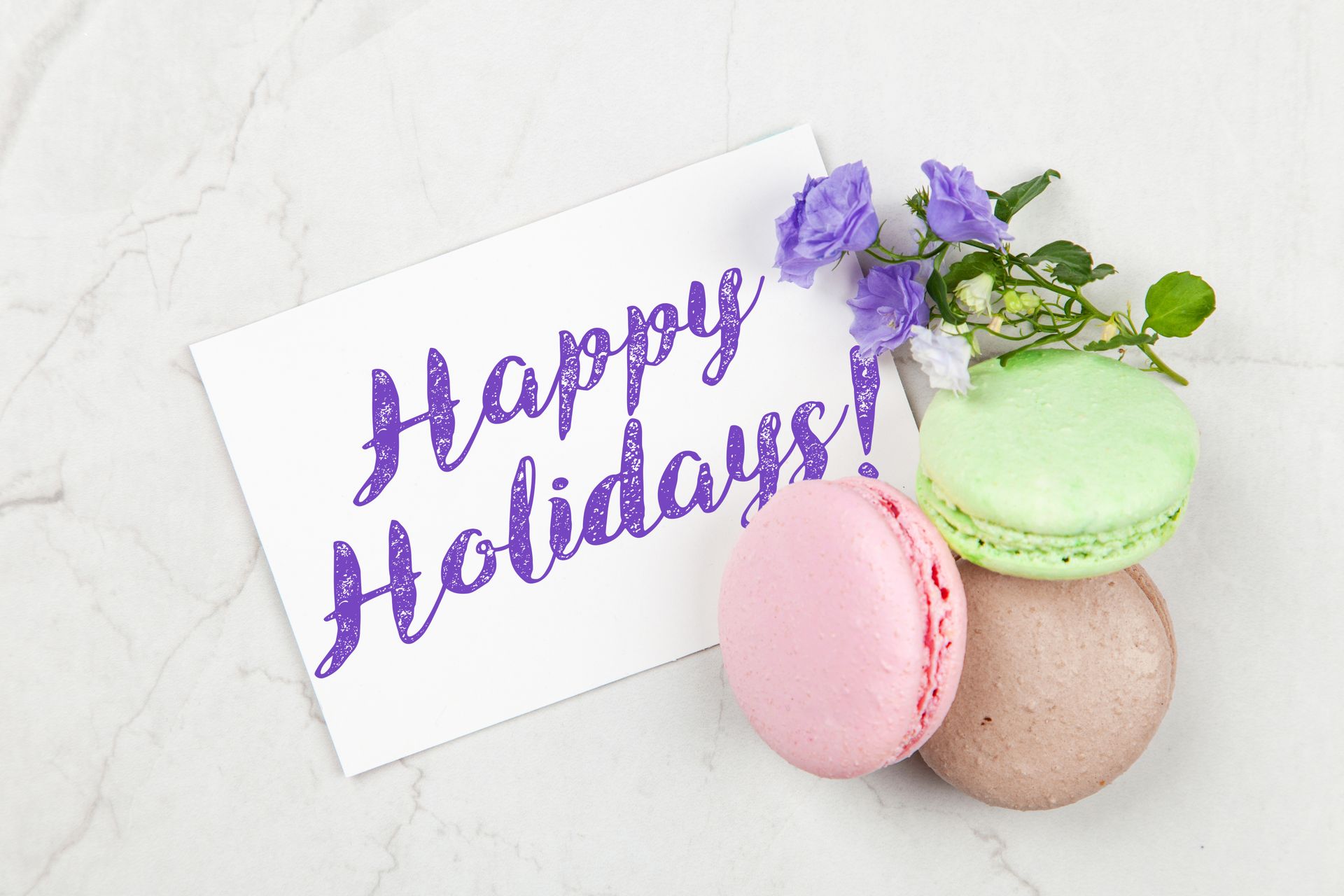 Bright and cheerful holiday greeting card with colorful flowers and macarons on a white background.