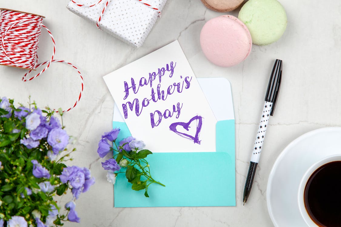 Free Happy Mothers Day Card Beside Pen, Macaroons, Flowers, and Box Near Coffee Cup With Saucer Stock Photo